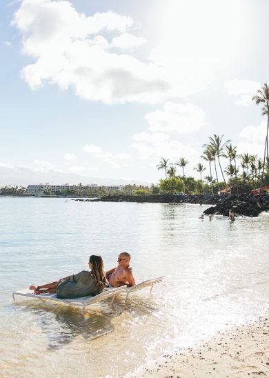 A serene beach scene with a woman and child on a surfboard, surrounded by calm water and palm trees under a bright sky.