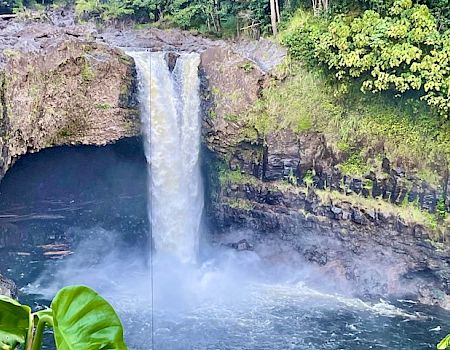 The image features a cascading waterfall surrounded by lush greenery and rocky terrain, creating a serene natural scene.