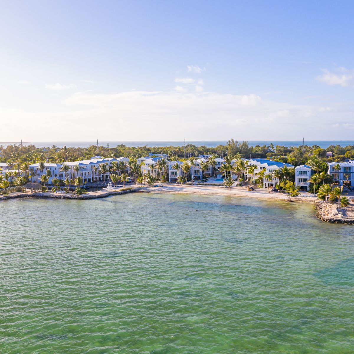 The image shows a scenic coastal view with clear water, land, and buildings near the shore under a bright sky.