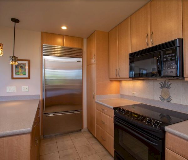 The image shows a modern kitchen with wooden cabinets, a stainless steel fridge, microwave, and an electric stove.