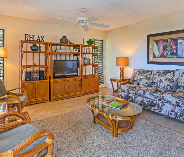 The image shows a cozy living room with a tropical theme, featuring comfortable furniture, a TV, and warm lighting.