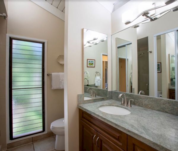 The image shows a modern bathroom with a sink, wooden cabinetry, a toilet, and large windows providing natural light.