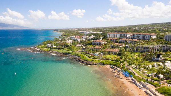 The image shows a scenic coastal view with clear blue water, sandy beaches, and lush green landscapes, likely a resort area.