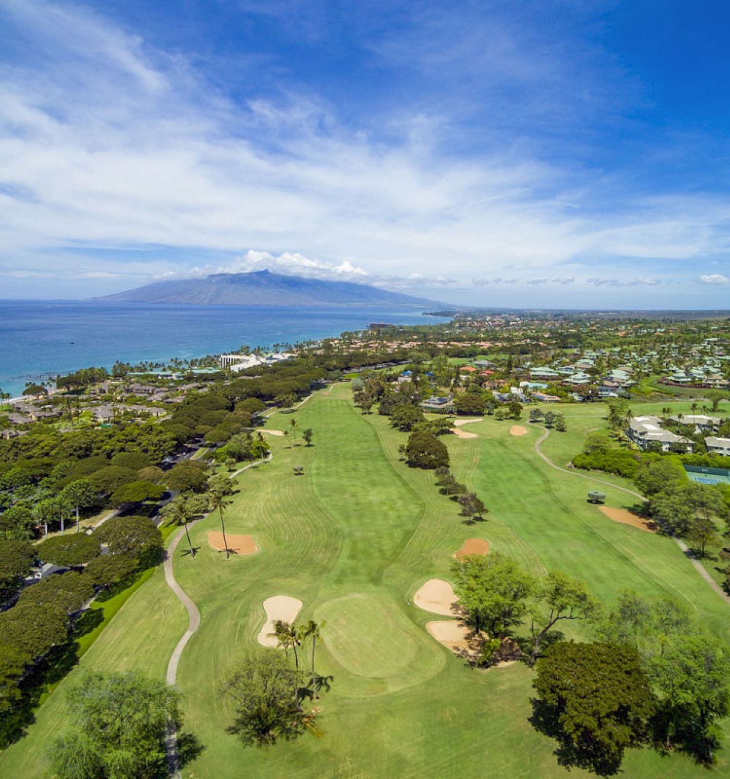 The image shows a scenic view of a golf course near a coastline, with lush greenery and mountains in the background.