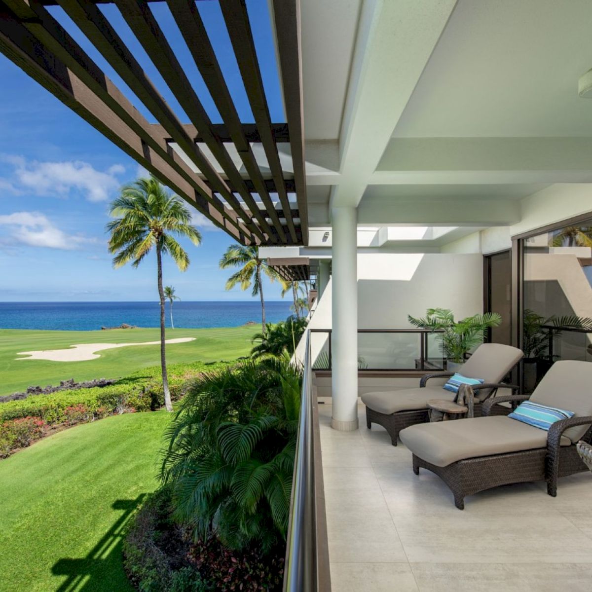 The image features a balcony overlooking a lush golf course and ocean, with comfortable loungers and clear blue skies.