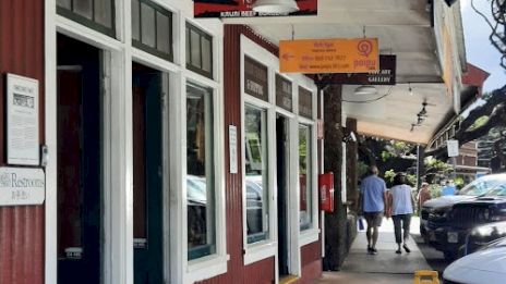 The image shows a street scene with storefronts, pedestrians walking, and a caution sign on the ground. It feels lively and urban.