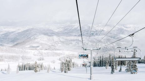 The image shows a snowy landscape viewed from a ski lift, with mountains and trees blanketed in white, creating a serene winter scene.