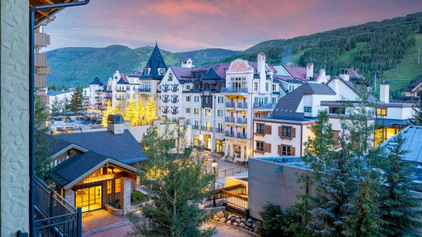 The image features a scenic view of a charming village with mountainous surroundings and a colorful sunset sky.