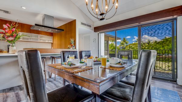 A stylish dining area features a wooden table set with meals, surrounded by black chairs and bright natural light from large windows.