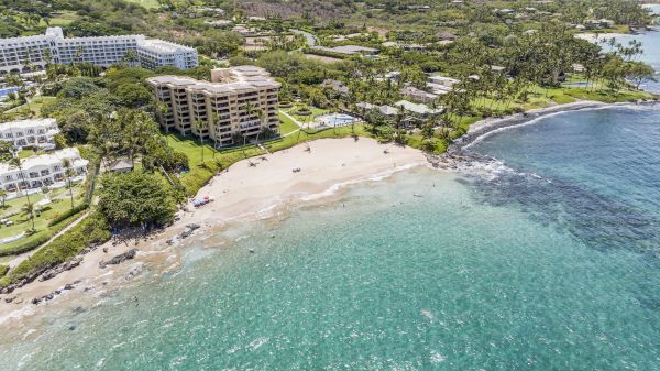The image shows a scenic coastal view with green landscapes, hotels, and a sandy beach merging into clear blue waters.