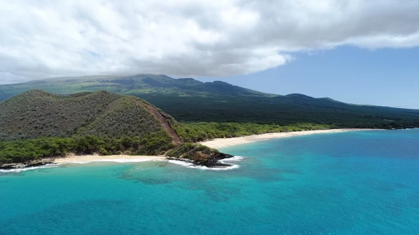A scenic beach with turquoise waters and lush green hills under a partly cloudy sky is depicted in the image.
