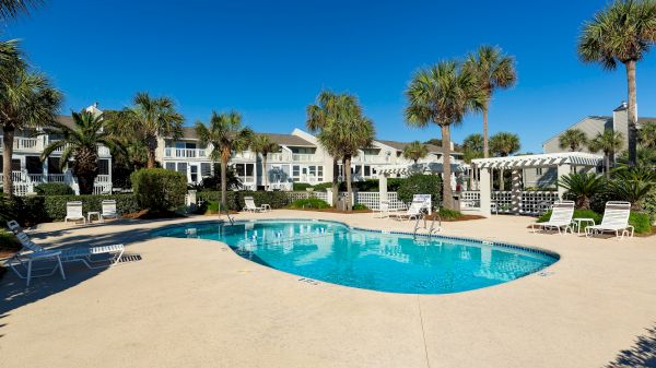 A swimming pool with lounge chairs, surrounded by palm trees and residential buildings under a clear blue sky.