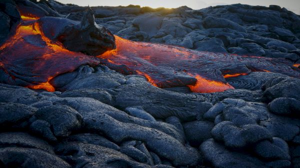 The image shows glowing lava flowing over dark, solidified rock, creating a striking contrast in a volcanic landscape.