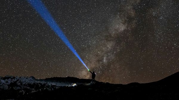 A person shines a blue flashlight into a starry sky, with the Milky Way galaxy visible in the background.