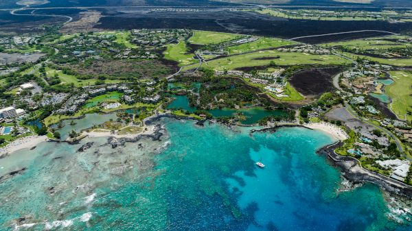 Aerial view of a coastal landscape with turquoise waters, lush greenery, and scattered buildings near the shoreline.