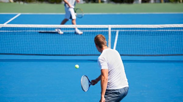 Two people are playing tennis on a blue court, focusing on a rally near the net.