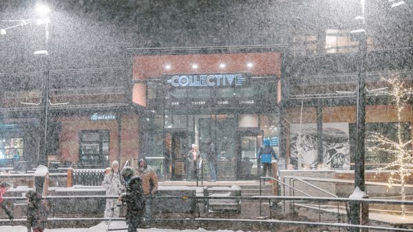 People in snowy weather outside a building labeled "Collective," with bright lights illuminating the scene.