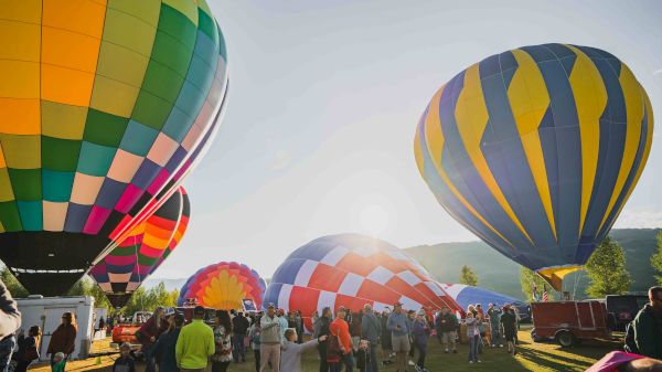 Colorful hot air balloons being inflated with a crowd of people gathered around in a field under a clear, sunny sky.