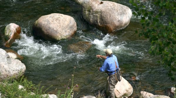 A person is fly fishing in a rocky river, wearing outdoor gear.
