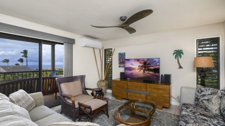 A cozy living room with a tropical theme features a TV, ceiling fan, and ocean view balcony.