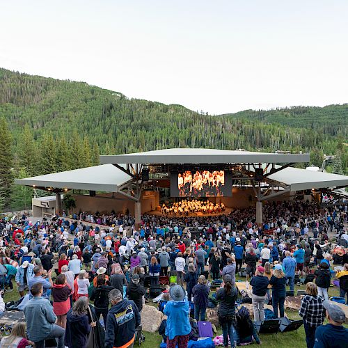 An outdoor concert amidst lush green hills, with a large audience gathered around a stage.