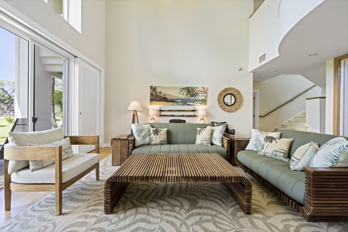 A modern living room with light furniture, a large window, patterned rug, and artwork on the wall, creating an airy and inviting space.