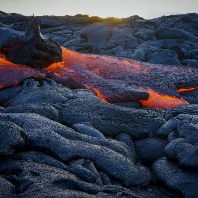 Molten lava is flowing over dark, hardened rocks, creating a striking contrast in colors and textures in the landscape.