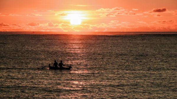 A picturesque sunset over the ocean with a silhouetted boat carrying people, creating a calm and tranquil scene.