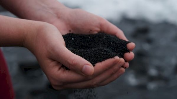 Two hands holding black sand against a blurred outdoor background.