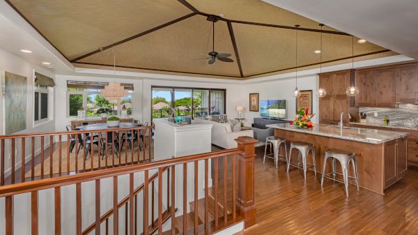 The image shows a spacious open-concept living area with a kitchen, dining area, and seating space, featuring wood accents and ceiling fans.