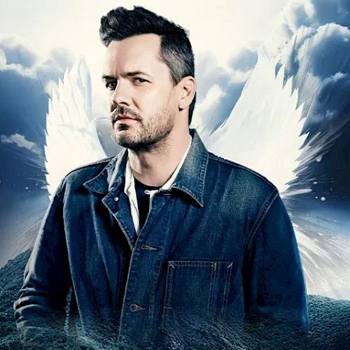 A man in a denim jacket is highlighted against a backdrop with clouds and angel wings, exuding a dramatic and mystical atmosphere.