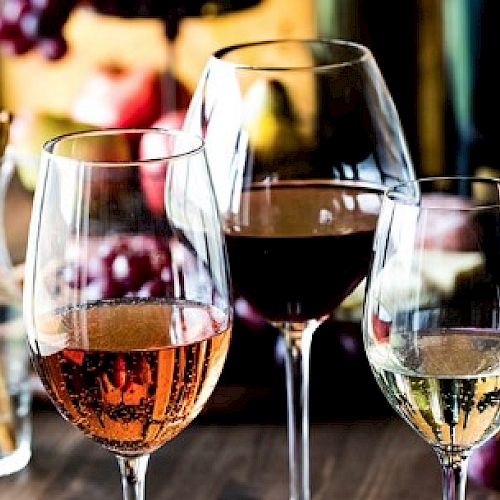 Three wine glasses with rose, red, and white wine are on a table, accompanied by breadsticks and grapes, creating a cozy ambiance.