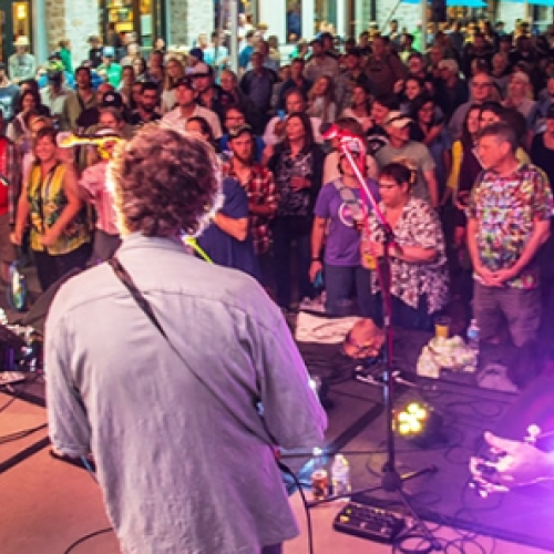 A band performs on stage to a large crowd at an outdoor event, with people enjoying the lively atmosphere.