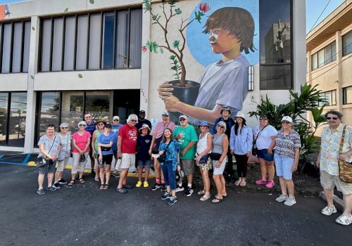 A group of people stands in front of a building, featuring a mural of a child holding a plant.