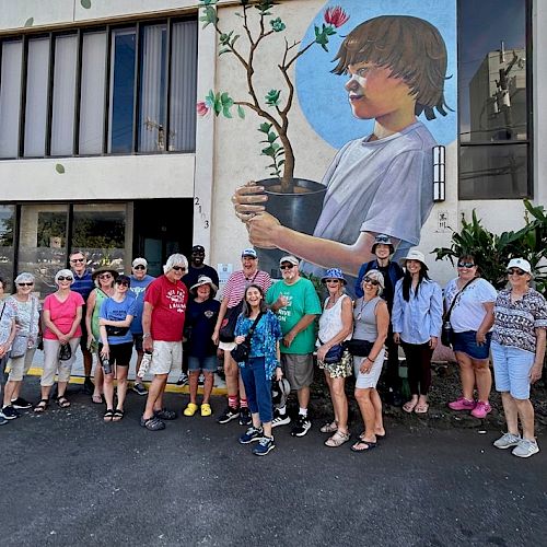 A group of people stands in front of a building, featuring a mural of a child holding a plant.