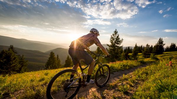 A person is mountain biking on a trail with a scenic view of hills and trees during sunset.