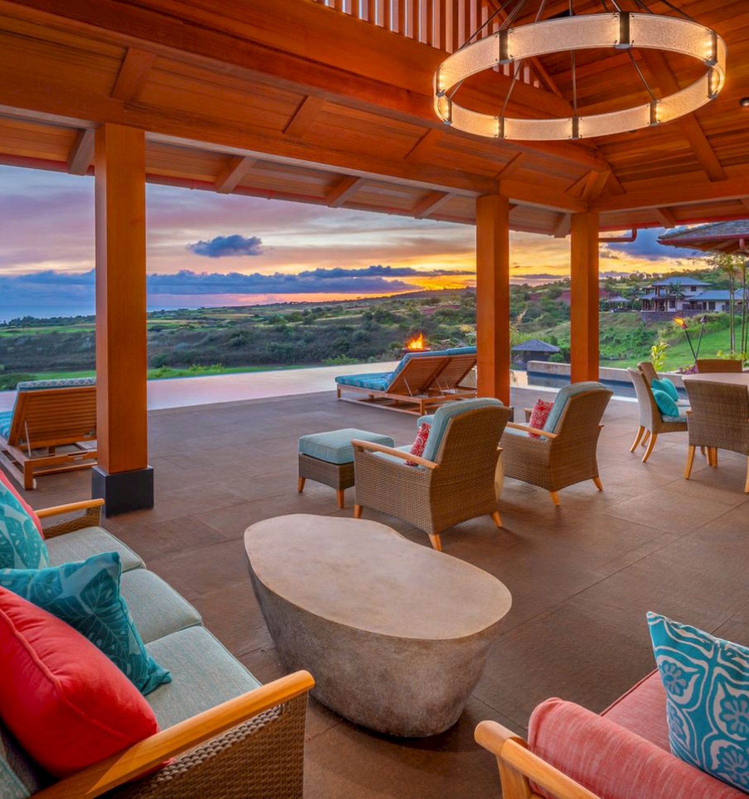 A luxurious outdoor patio with comfortable seating, colorful cushions, and a scenic view of a sunset over a vast landscape.