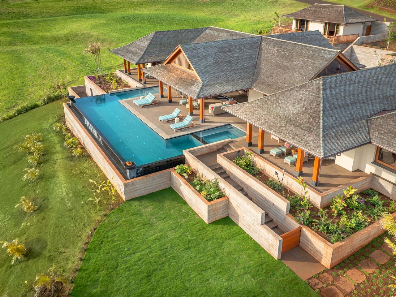 Luxurious villa with infinity pool, sun loungers, and landscaped garden set in a lush green environment.