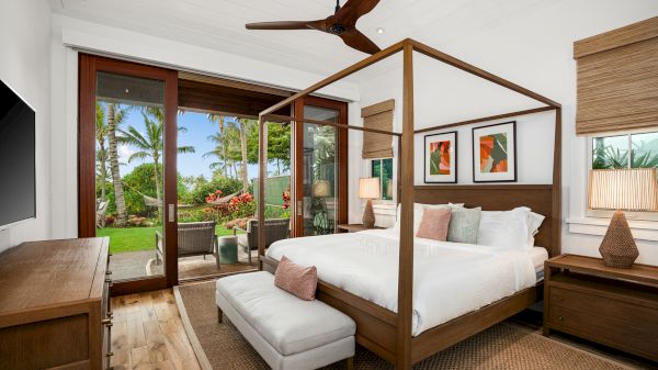 A bright bedroom with a canopy bed, wooden furniture, and tropical views through sliding glass doors ending the sentence.