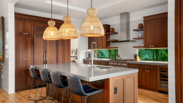 A modern kitchen with wooden cabinetry, an island with seating, pendant lights, and a stainless steel faucet.