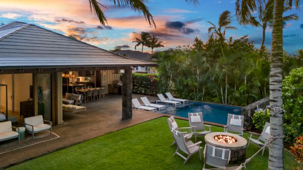 A tropical outdoor setting with a patio, pool, fire pit, and hammock, surrounded by palm trees at sunset.