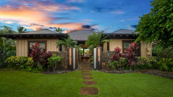 A tropical house with lush landscaping and a stone path under a colorful sky.