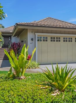 A tidy single-family home with a three-car garage, tropical landscaping, and a bright, sunny sky; concrete driveway leads to the garage.