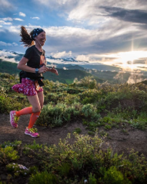 A person is running on a trail surrounded by lush greenery, with a dramatic sunset in the background.