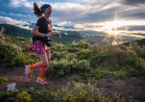 A person is running on a trail surrounded by lush greenery, with a dramatic sunset in the background.