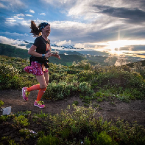 A person is running on a trail surrounded by lush greenery, with a dramatic sunset in the background.