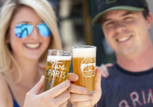 Two people are smiling and holding up glasses of beer for a cheers.