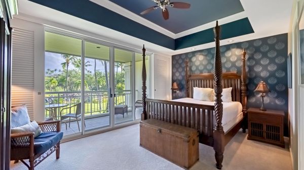 A bright, luxury hotel room with a four-poster bed, balcony view, ceiling fan, and blue-accented decor.
