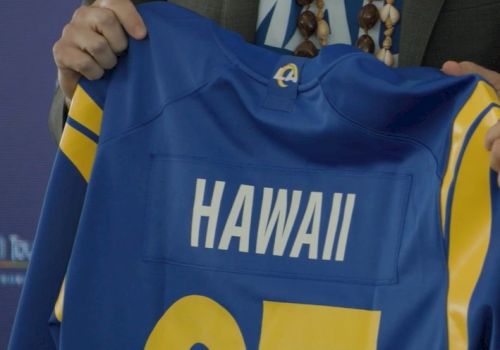 A person holds a blue sports jersey with "HAWAII" and the number 25 on it, likely from a team affiliated with Los Angeles.