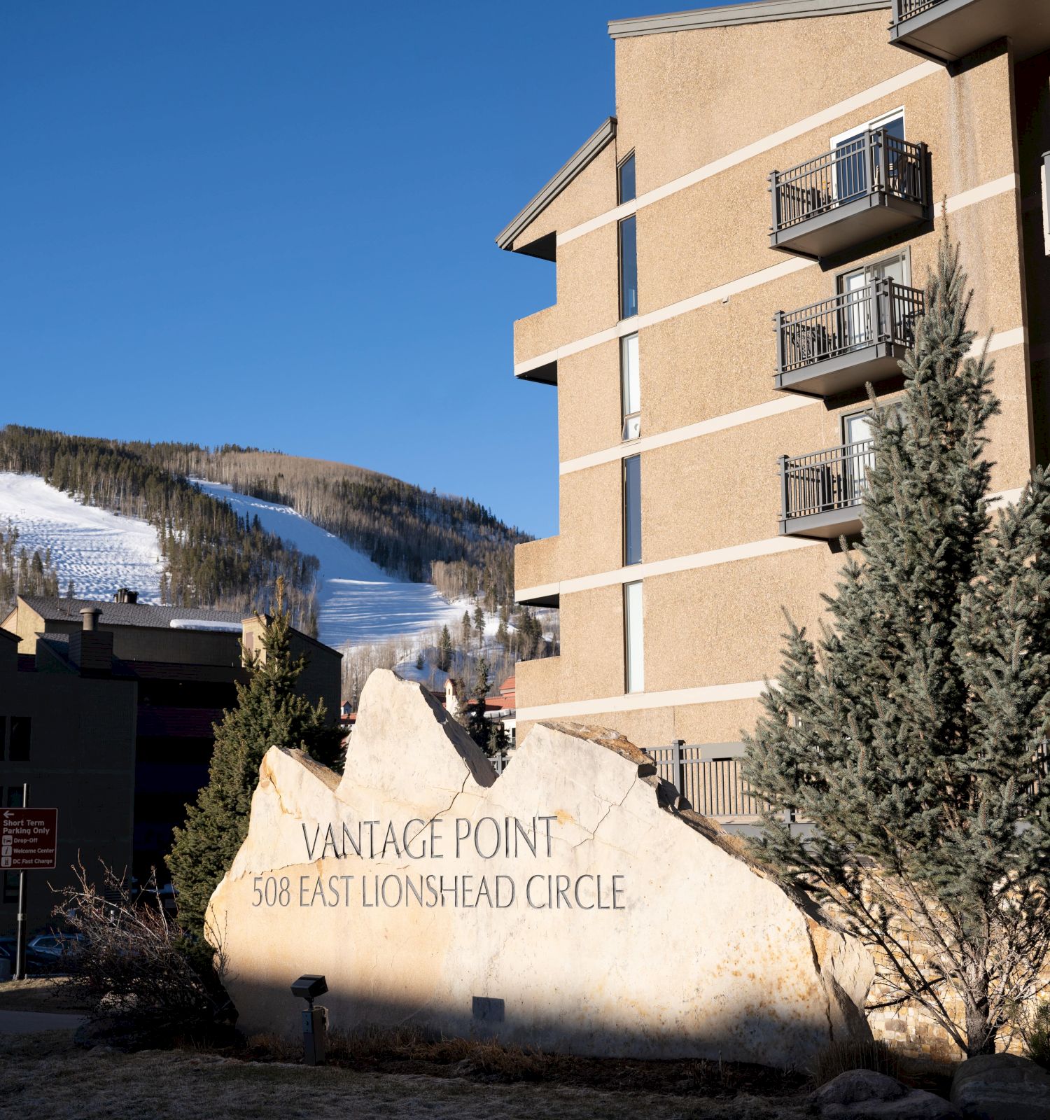 The image shows a building complex with a stone sign reading "Vantage Point 508 East Lionshead Circle" and a snowy mountain in the background.